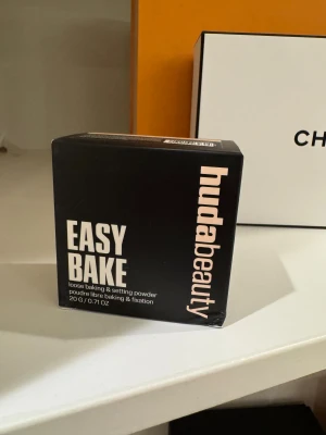 Huda Beauty Easy Bake Cupcake puder - Loose baking & setting powder från Huda Beauty i nyansen Cupcake. Kommer i en svart fyrkantig förpackning med ljusrosa text. Perfekt för att fixera sminket och ge en matt finish. Innehåller 20g puder.