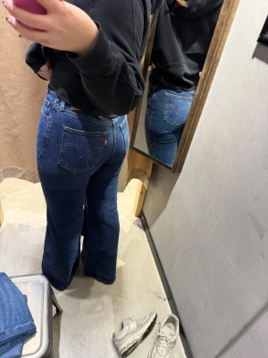 Levis Ribcage Bell  - Säljer ett par klassiska blå Levi's jeans med bootcut passform och hög midja. Jeansen har tydliga bakfickor med den ikoniska Levi's-loggan och är tillverkade i slitstarkt denim. Perfekt för dig som gillar retrovibbar och vill ha ett snyggt snitt.