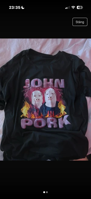 Svart John Pork t-shirt med tryck - Cool svart t-shirt med stort John Pork-tryck på framsidan, med eld och blixtar i motivet. T-shirten har rund hals och är kortärmad. Materialet är mjukt och stretchigt, tillverkat av 95% polyester och 5% elastan. Perfekt för dig som gillar unika och trendiga prints.