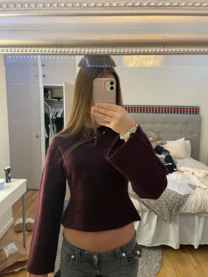 Vinröd stickad tröja från Gina 14+ - Superfin och ny vinröd stickad tröja från Gina 14+. Croppad modell med breda, långa ärmar och rund halsringning. Mjuk och fluffig känsla, perfekt för att ge din outfit en mysig vibe. Passar dig som gillar trendiga och bekväma plagg med lite extra attityd.