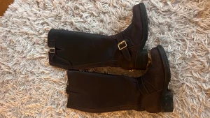 Bruna stövlar från Johnny Bulls skinn - Säljer ett par bruna stövlar från Johnny Bulls i skinn med grov sula, guldfärgade spännen och dragkedja på sidan. Klassisk modell med låg klack och robust känsla, perfekta för dig som gillar stilrena boots med detaljer.