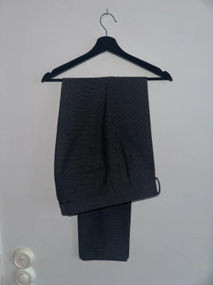 Grå kostymbyxor från Hugo Boss - Snygga grå kostymbyxor från Hugo med diskret rutig struktur. Klassisk rak passform och stilrena fickor. Perfekt för dig som vill ha en clean och modern look. Materialet känns mjukt och har en exklusiv känsla.