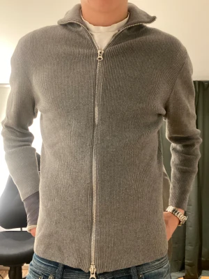 Ljusgrå Cardigan/kofta från Ljung Marcus Larsson - Säljer en stilren grå kofta från Ljung Marcus Larsson i storlek M. Den är endast använd ett par gånger och är därför i mycket fint skick. Perfekt att slänga på över en t-shirt för en chill look. Snygg krage och klassisk passform. Nypris: 1499