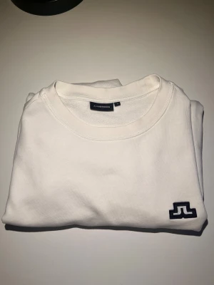 Vit sweatshirt från J.Lindeberg M - Vit sweatshirt från J.Lindeberg i klassisk modell med rund hals och svart broderad logga på bröstet. Bra skick