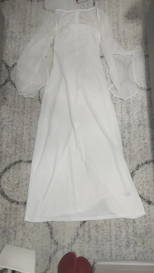 Vit långklänning med pärldetaljer - Superfin vit långklänning med transparenta puffärmar dekorerade med små pärlor. Klänningen har en figurnära passform och fyrkantig urringning. Materialet är tunt och flowy, vilket ger en elegant känsla. Perfekt för dig som vill sticka ut med en stilren look.