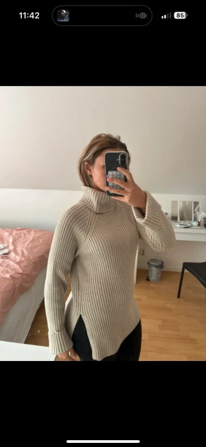 Beige ribbad polotröja med slits - Säljer en beige polotröja med ribbad struktur och höga slitsar på sidorna. Tröjan har lång ärm och en bred polokrage som ger extra mysig känsla. Perfekt för dig som gillar en loose fit och vill ha något som sticker ut lite i garderoben.