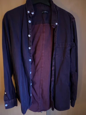 Mörklila skjorta från Jack & Jones - Snygg mörklila skjorta från Jack & Jones med klassisk krage och vita knappar. Skjortan har en bröstficka och är tillverkad i mjuk bomull. Perfekt för dig som gillar stilrena och enkla plagg med lite edge.