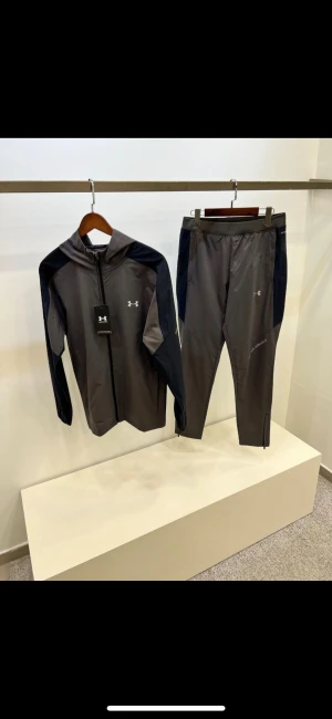 Grå träningsbyxor från Under Armour - Snygga grå träningsbyxor från Under Armour med svarta paneler längs sidorna. Byxorna har smal passform, elastisk midja och dragkedja vid benslut. Perfekta för gymmet eller löprundan, tillverkade i lätt syntetmaterial som andas.