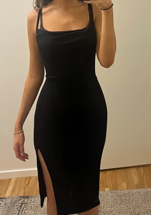 Svart midi klänning med slits - Snygg svart midi klänning med smala axelband och en stilren, rak siluett. Klänningen har en elegant slits på ena sidan och en lätt draperad urringning. 