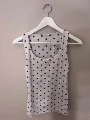 Vit prickig linnetopp från Zara - Säljer en vit linnetopp från Zara med svarta prickar. Toppen är ärmlös och har en klassisk rund halsringning. Materialet är mjukt och strechigt 