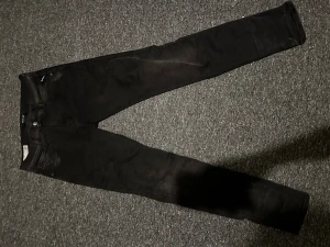 Svarta Replay Anbass jeans slim fit - Svarta Replay Anbass jeans i slim fit med klassisk femficksdesign och snygga detaljer på bakfickorna. Jeansen är tillverkade i stretchigt denim och har en stilren look med svarta sömmar och Replay-logga på läderpatchen bak i midjan. W30 L32