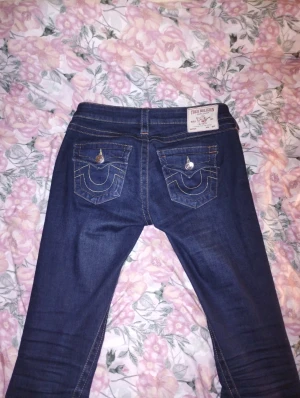 True Religion jeans - True Religion med ikoniska fickor bak och silverfärgade knappar. Klassisk passform och kontrastsömmar ger en cool look. Perfekta för dig som vill sticka ut med detaljerad design och exklusivt märke.