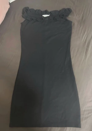 Svart klänning med volang - Svart långklänning från med volangdetalj upptill. Klänningen har en tight passform