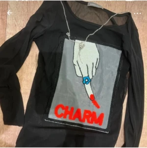 Svart meshtröja med print från Unice - Cool svart meshtröja från Unice med lång ärm och ett stort print framtill av en hand med blå ring och röd texten 'CHARM'. Tröjan har en transparent känsla och passar perfekt för dig som vill sticka ut.