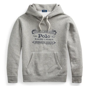Grå hoodie från Polo Ralph Lauren - Snygg grå hoodie från Polo Ralph Lauren med mörkblå tryck framtill. Tröjan har huva med snörning och en stor magficka. Perfekt för chill dagar och enkel att matcha med jeans eller joggers.
