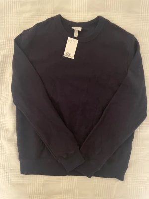 Mörkblå stickad tröja från H&M - En stilren mörkblå stickad tröja från H&M i regular fit. Tröjan har rund halsringning, diskret strukturmönster och långa ärmar. Perfekt för lager-på-lager och enkel att matcha med jeans eller chinos.