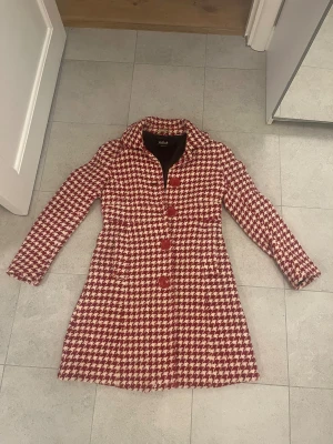 Rutig röd kappa från Killah - Säljer en snygg röd och vit rutig kappa från Killah i storlek medium. Jackan har stora röda knappar framtill och bak, klassisk krage och långärmad design. Materialet är tjockt och känns som ullblandning, perfekt för höst och vinter.
