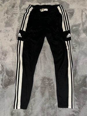  Adidas träningsbyxor  - Adidas träningsbyxor i svart med klassiska vita ränder längs sidorna och logga på låret. Modellen är slim fit med elastisk midja och tillverkad i polyester. Byxorna har AEROREADY-teknologi för att hålla dig torr och bekväm under träning. men det finns bra två lite hål.!