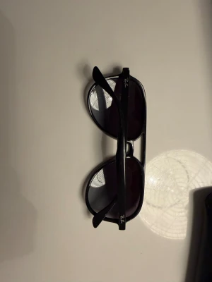 Svarta Ray-Ban pilotglasögon - Snygga svarta Ray-Ban solglasögon i klassisk pilotmodell med mörka glas. Ramen är i svart plast och loggan syns på bågen. Kommer med originalfodral och box. Perfekt för dig som vill ha en ikonisk look och skydda ögonen mot solen.