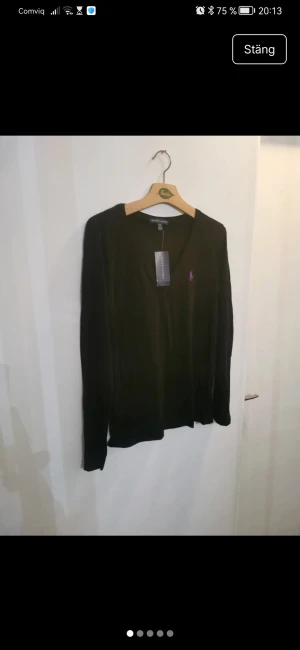 Svart v-ringad tröja Ralph Lauren M - Svart v-ringad tröja från Ralph Lauren i storlek M. Tröjan har lång ärm och är tillverkad i mjuk bomull. På bröstet finns den klassiska lila Ralph Lauren-loggan broderad. Perfekt för dig som gillar stilrena och enkla plagg med en touch av lyx.Väldigt fin tröja i helt ny skick. Material: 100 % bomull Tillverkar-ID: RN 41381 / CA 56658 (detta är registrerat till Ralph Lauren) Tvättråd: Maskintvätt kall, torktumling låg värme, kan strykas varmt