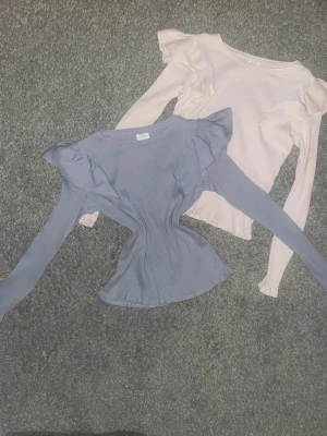 TVÅ Ribbad topp med volang från ZARA - Två snygga ribbade toppar från ZARA med volangdetaljer på axlarna. Ena toppen är ljusblå och den andra är vit, båda med lång ärm och figurnära passform. Perfekt för dig som gillar stilrena och trendiga plagg med extra detaljer. Så fin till fest eller vardag 💕