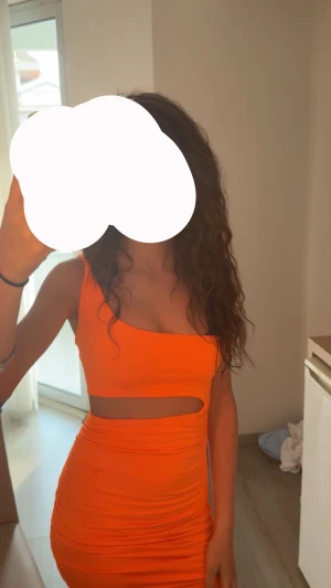 Orange tight klänning - Säljer en superfräsch orange tight kortklänning med cut out-detalj under bysten och asymmetrisk axel. Klänningen är ärmlös och har en figurnära passform. Perfekt för dig som vill sticka ut med en färgstark look!