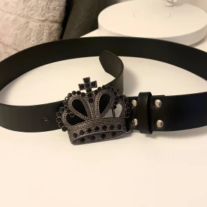 Bälte med krona - Coolt svart bälte med ett stort, detaljerat spänne i form av en krona dekorerad med svarta stenar. Ca 97 cm, köpt secondhand. 3 stenar saknas men syns inte. Skriv om ni har frågor 💕