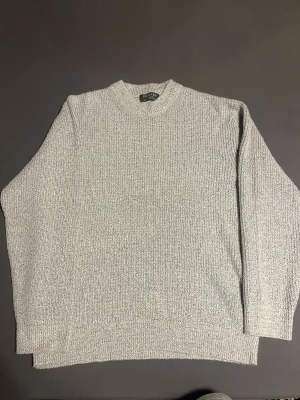 Grå stickad tröja från Primark - En stilren grå stickad tröja från Primark med rund hals och ribbade muddar. Tröjan har en klassisk passform och är perfekt för dig som gillar enkel och clean look. Materialet är mjukt och håller dig varm under kalla dagar. Passar dig som vill ha en basic och jätte mysig tröja. Priset diskuteras vid snabb affär.