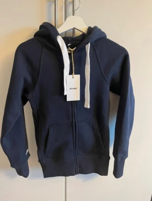 Marinblå hoodie från Russemarch XXS - Snygg marinblå hoodie från Russemarch i unisexmodell med vit snörning och dragkedja framtill. Tröjan har huva, två fickor och ribbade muddar. Aldrig andvänd endast testad då den är lite för liten för mig, org pris 749kr. Vid snabb affär kan priset diskuteras💕💕💕