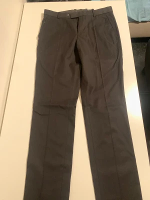 Svarta kostymbyxor H&M Slim Fit - Svarta kostymbyxor från H&M i slim fit-modell. Klassisk design med bälteshällor, snedställda fickor och rak siluett. Perfekt för dig som gillar stilrena och enkla byxor med smal passform. Materialet är mjukt och har en lätt glans.