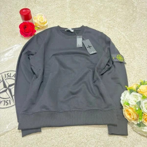 Svart sweatshirt från Stone Island - Svart sweatshirt från Stone Island med klassisk rund hals och ribbade muddar. Tröjan har den ikoniska loggan på vänster ärm och är tillverkad i mjuk bomull. Perfekt för dig som gillar stilrena och trendiga plagg.