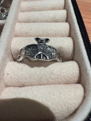 Silvrig ring med fladdermusdesign - Unik silvrig ring med en detaljerad fladdermus som motiv. Ringen har öppningsbar design och är tillverkad i metall med snygga graveringar som framhäver vingarna och kroppen på fladdermusen. Perfekt för dig som gillar djurmotiv och vill sticka ut med din stil.