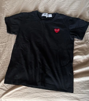 Svart Comme des Garçons Play t-shirt XS - Svart t-shirt från Comme des Garçons Play med det ikoniska röda hjärtat broderat på bröstet. Klassisk rund halsringning och korta ärmar. Skön passform i mjuk bomull, perfekt för en clean och stilren look. Skrivit XS i storlek för den här krympt i i tvätten. Använd få gånger bra skick