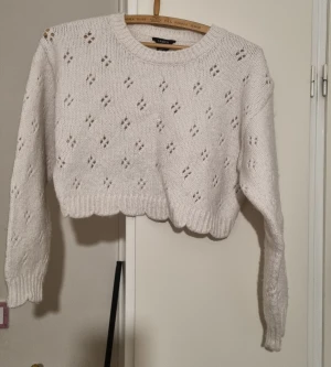 Vit croppad stickad tröja Lindex - Superfin vit stickad tröja från Lindex med hålmönster och croppad passform. Tröjan har långa ärmar, rund halsringning och ribbade muddar. Perfekt för lager-på-lager och snygg till både jeans och kjol.