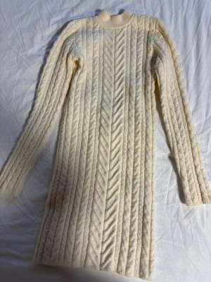 Stickad vit klänning från Bershka - Superfin stickad klänning från Bershka i beige färg med kabelstickat mönster. Långärmad modell med hög hals och en snygg öppen rygg som ger en cool twist. Perfekt för dig som gillar mysiga men ändå trendiga outfits. Superfint skick! 100kr☁️