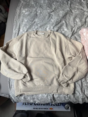 Beige sweatshirt från Gina Tricot M - Säljer en stilren beige Gina Tricot från Amaztricot i storlek M. Tröjan har rund hals, ribbade muddar vid ärmslut och nederkant samt en mjuk insida. Perfekt för chill dagar och enkel att matcha med jeans eller mjukisbyxor.