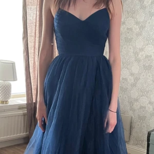 Marinblå balklänning - Marinblå klänning med puffig kjol och knyt i ryggen. Aldrig använd. Perfekt för bal.