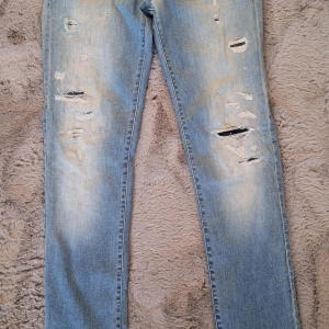 Replay Rose ljusa ripped jeans 29/32 - Säljer ett par ljusblå jeans från Replay, modell Rose, med snygga slitningar och ripped detaljer framtill. Klassisk femficksdesign, knappstängning och coolt Replay-märke vid fickan. Perfekt för dig som gillar en avslappnad streetstil.