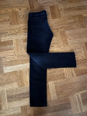 Svarta jeans från Nudie Jeans - Säljer ett par svarta jeans från Nudie Jeans med klassisk femficksdesign och snygga kontrastsömmar på bakfickorna. Jeansen har normal passform och raka ben, tillverkade i mjukt och slitstarkt bomullsmaterial. Perfekta för dig som gillar stilrena och tidlösa jeans. Storlek W32 L30