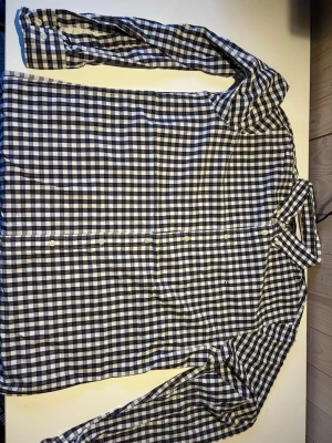 Rutig skjorta Tommy Hilfiger Slim Fit L - Snygg rutig skjorta från Tommy Hilfiger i storlek L, slim fit. Skjortan har klassiskt rutmönster i marinblått, vitt och röda detaljer, med knappar framtill och lång ärm. Tillverkad i mjuk bomull och har diskret logga broderad på bröstet.