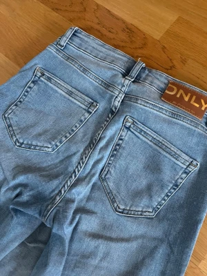 Bootcut jeans från ONLY i ljusblå denim - Säljer ett par snygga ljusblå bootcut jeans från ONLY. Klassisk femficksmodell med normal passform och medelhög midja. Jeansen är tillverkade i mjuk denim med dragkedja och knapp framtill. Perfekta för dig som gillar retrovibbar och vill ha ett par bekväma jeans.