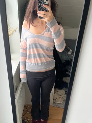 Tröja - Säljer en mjuk och skön långärmad tröja från Fred Perry med breda rosa och grå ränder. Tröjan har v-ringning, avslappnad passform och broderad logga på bröstet.