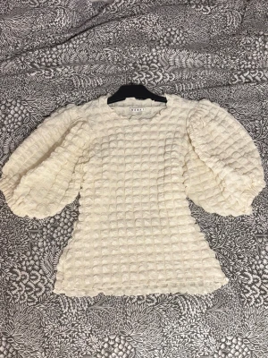 Vit strukturerad blus från Wera - Säljer en superfin vit blus från Wera med puffiga långärmar och ett unikt rutigt, strukturerat tyg. Blusen har en lätt vågig kant vid halsen och är perfekt för dig som gillar statement-ärmar och cool textur.