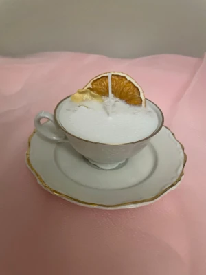 Doftljus utav vanilj i en vitt tekopp  - Det här ljuset är gjort av återanvändbara material. Tekoppen är köpt secondhand och stearinet är från kyrkor som tänkte slänga det. Det här ljuset har en svag doft utav vanilj, så känsliga även kan använda det. Det här ljuset har även torkade blommor och torkad apelsin på som dekoration. 