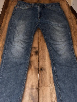 Levi's 511 blå jeans W34 L34 - Säljer ett par klassiska Levi's 511 jeans i blå tvätt med snyggt slitna detaljer. Modellen har normal passform med raka ben och fem fickor. Tillverkade i tåligt jeanstyg med den ikoniska röda Levi's-lappen på bakfickan och läderpatch i midjan.