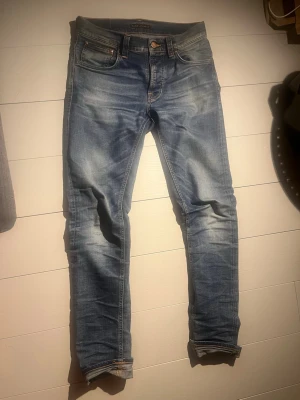 Nudie Jeans - Säljer ett par klassiska blå jeans från Nudie Jeans i straight passform. Jeansen har snygga slitningar och kontrastsömmar, fem fickor och knappgylf. Tveka inte på att höra av er vid frågor!