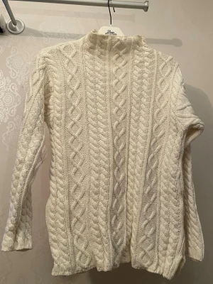 Vit stickad polotröja med flätmönster - Säljer en mysig vit stickad polotröja med klassiskt flätmönster. Tröjan har hög hals och långa ärmar.