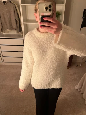 Fluffig vit stickad tröja - Supermjuk och fluffig vit stickad tröja med rund hals och långa ärmar. Tröjan har en oversized känsla och är perfekt för kyliga dagar. Ribbstickad kant nedtill och vid ärmslut för extra mysfaktor.