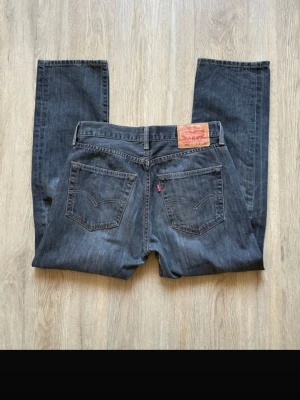 Levi's 501 mörkblå jeans W31 L30 - Klassiska Levi's 501 jeans i mörkblå tvätt med raka ben och knappgylf. Jeansen har fem fickor, tydliga sömmar och den ikoniska röda Levi's-lappen på bakfickan. Tillverkade i slitstarkt bomullsjeansmaterial. Perfekta för en avslappnad och tidlös look.