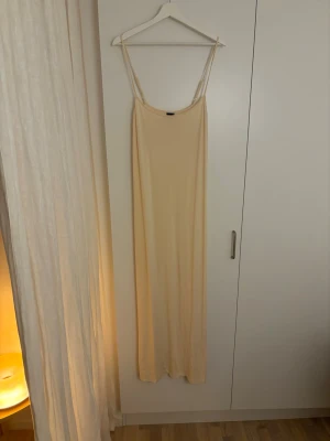 Ljusgul långklänning med smala axelband - Säljer en enkel och stilren långklänning i ljusgul ton. Klänningen har smala justerbara axelband och rak passform som faller snyggt längs kroppen. Materialet känns mjukt och lätt, perfekt för varma dagar. Passar dig som gillar minimalistisk och clean stil.